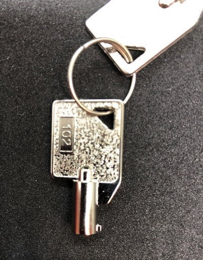 Close-up of a silver Key 102 with the number "192" engraved, attached to a key ring and a rectangular metal tag, reminiscent of an old AED Shop stamped key.