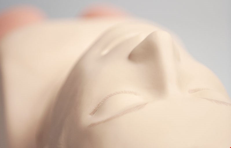 Close-up of a smooth, light-colored Airway Management Trainer Laerdal head from Laerdal, lying on its back, showing its nose and closed eyes.