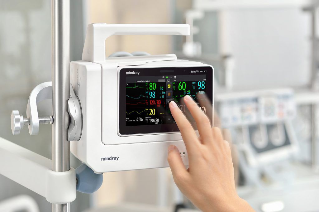A hand touches the touchscreen display of a pole-mounted Mindray BeneVision N1 patient monitor.