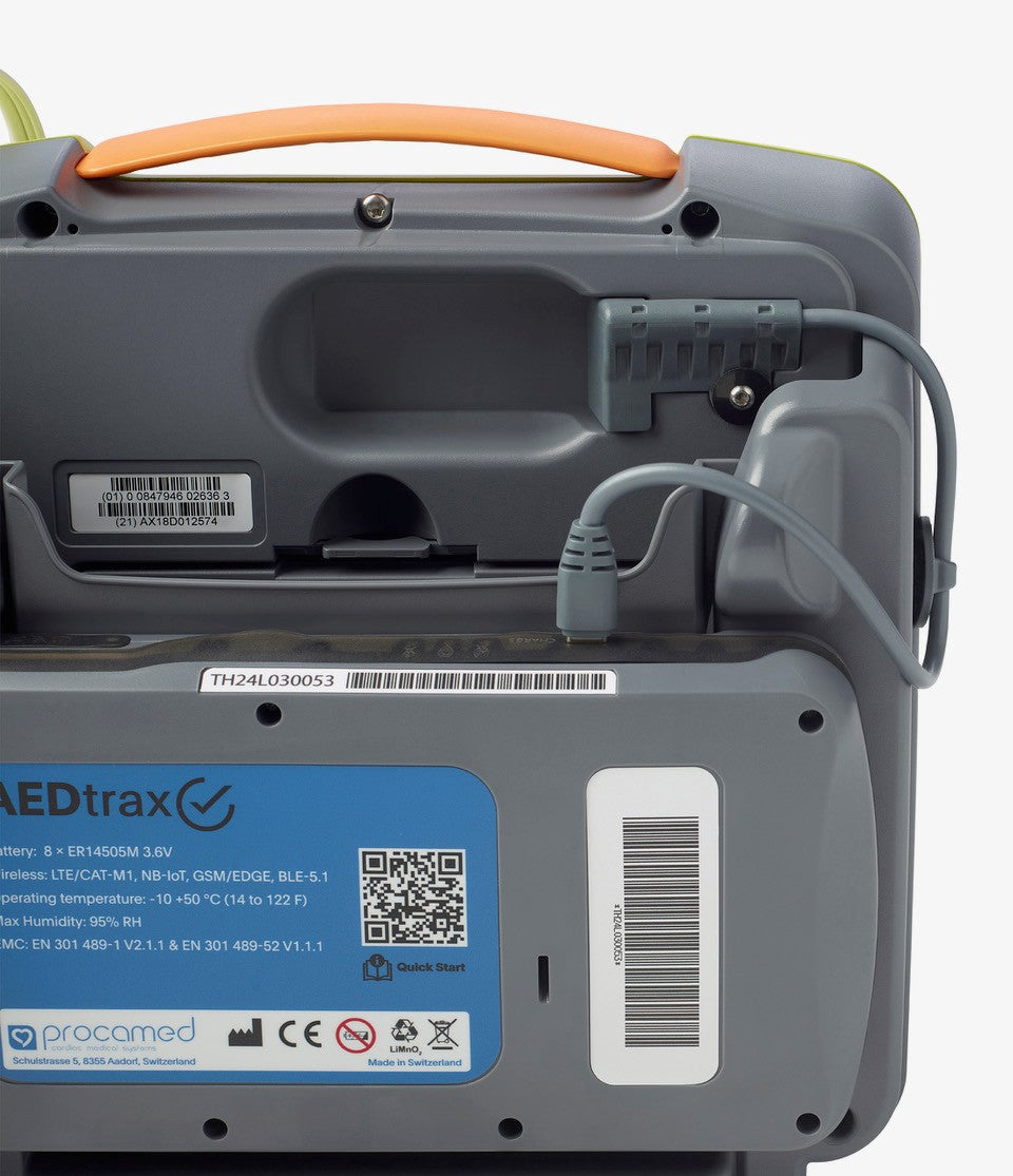 Back view of The AED Shop's AEDtrax device showing cables, ports, labels, a blue instruction sticker, and AED monitoring features.