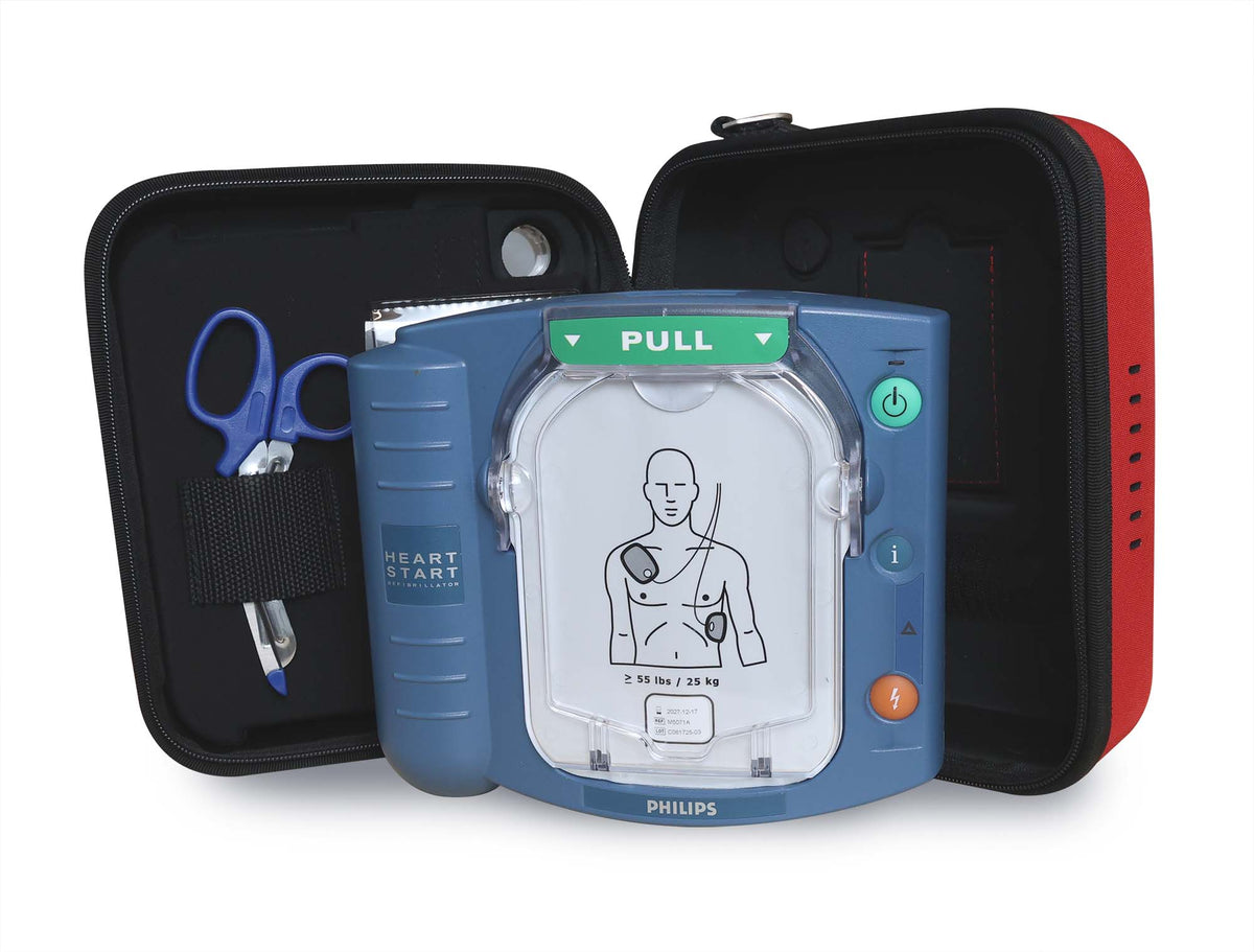 A Philips HeartStart OnSite Defibrillator by Philips is shown in an open case with scissors, displaying the electrode pad placement diagram on its screen.