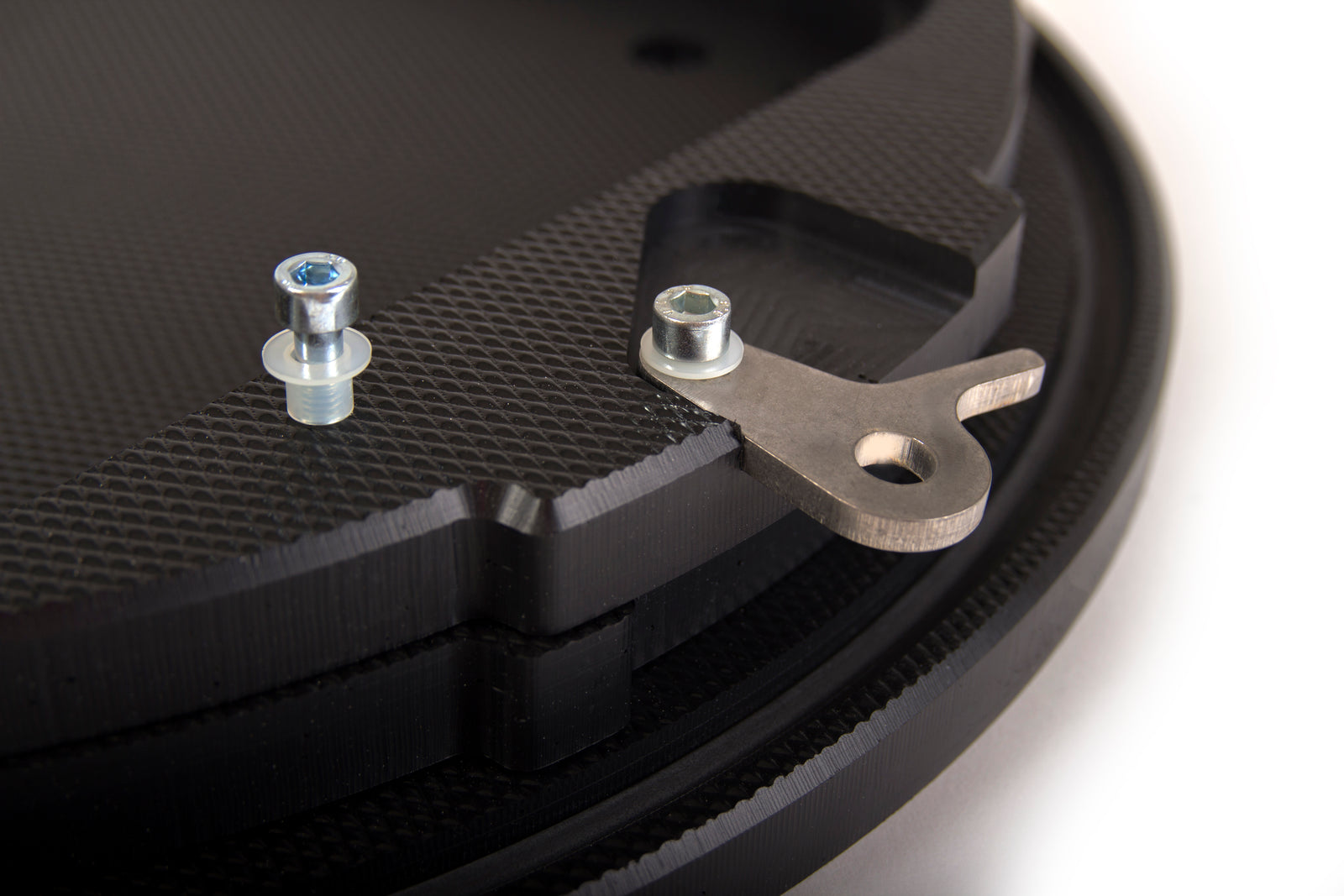 Close-up of a black textured component, likely part of the durable Rotaid Solid Plus AED Cabinet with Alarm, showcasing two screws and a metal bracket attached, all set against a white background.